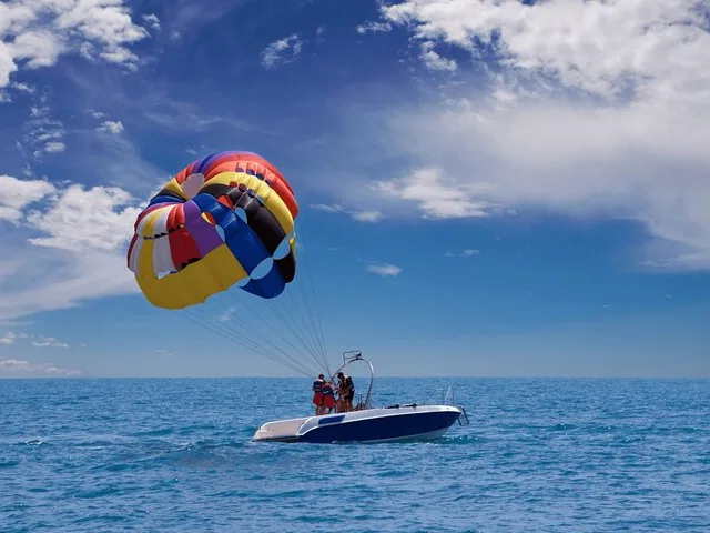 People parasailing over the ocean, pulled by a small blue and white speedboat
