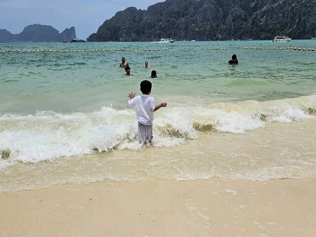 Un bambino sta su una spiaggia sabbiosa e guarda onde delicate, con le montagne sullo sfondo