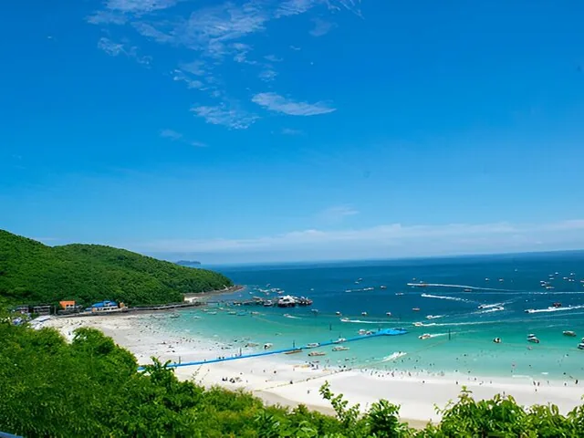 A scenic view of a curved beach with bright blue water and boats docked at a pier