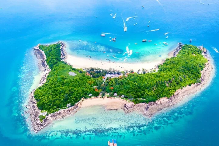 Una perspectiva aérea de una isla verde con una destacada playa de arena y barcos alrededor.