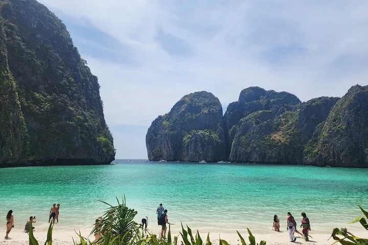 Turisti su una spiaggia di sabbia bianca circondata da imponenti scogliere calcaree a Maya Bay